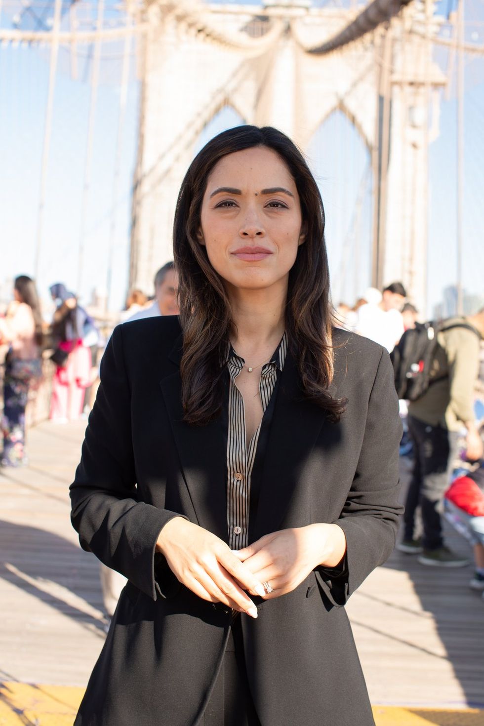 carlina rivera poses on the brooklyn bridge wearing a black blazer and a pinstriped button up