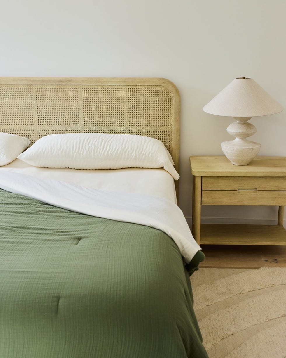 a neatly made bed with a green quilt pillows and a bedside table with a lamp