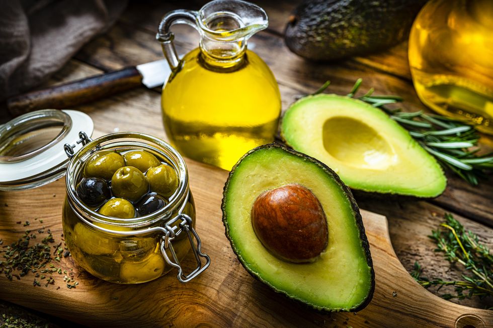 vegan food high angle view of extra virgin olive oil and avocado oil shot on rustic wooden table sliced organic avocado and a glass container with olives complete the composition predominant colors are yellow and green high resolution 42mp studio digital capture taken with sony a7rii and sony fe 90mm f28 macro g oss lens
