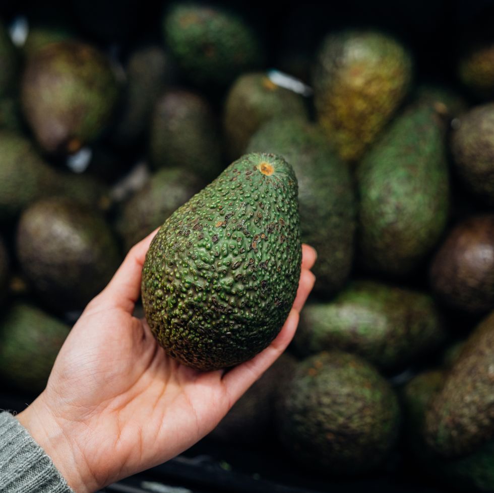 woman choosing avocados in supermarket