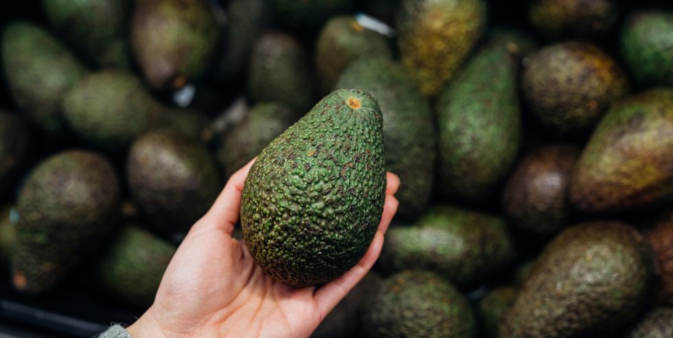 woman choosing avocados in supermarket