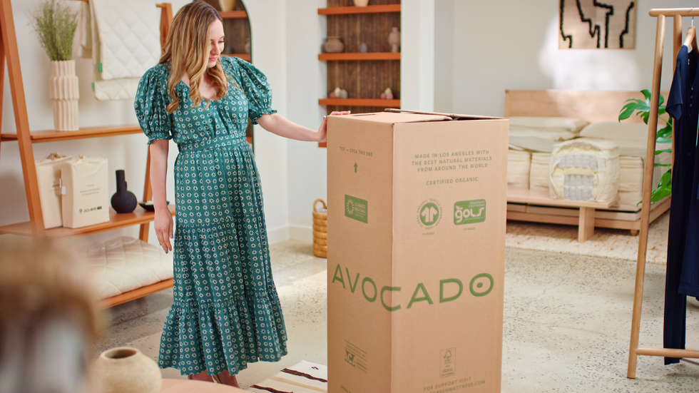 a woman in a dress holding a large mattress box