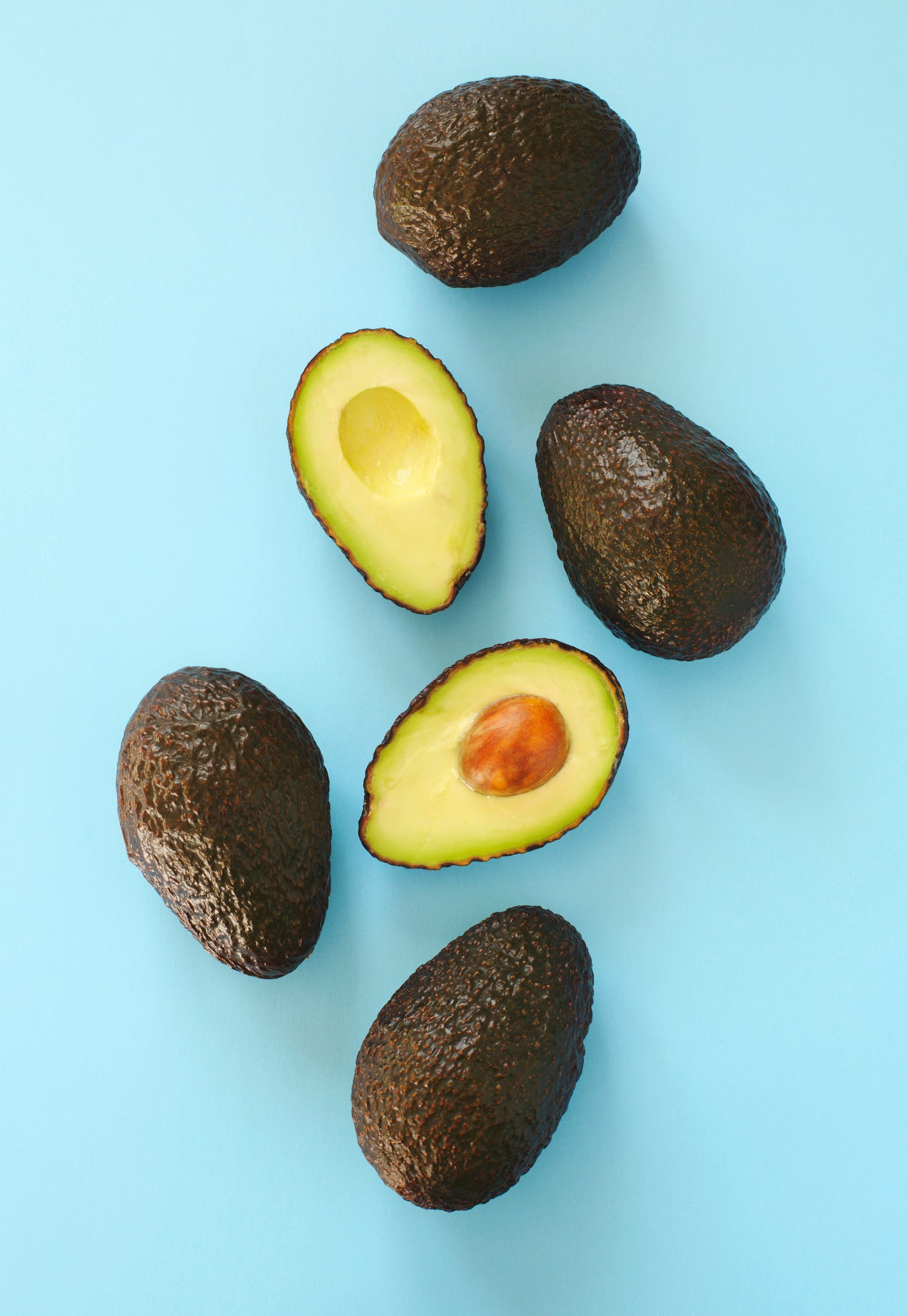 Avocado halves and whole on a blue speckle, top viev.