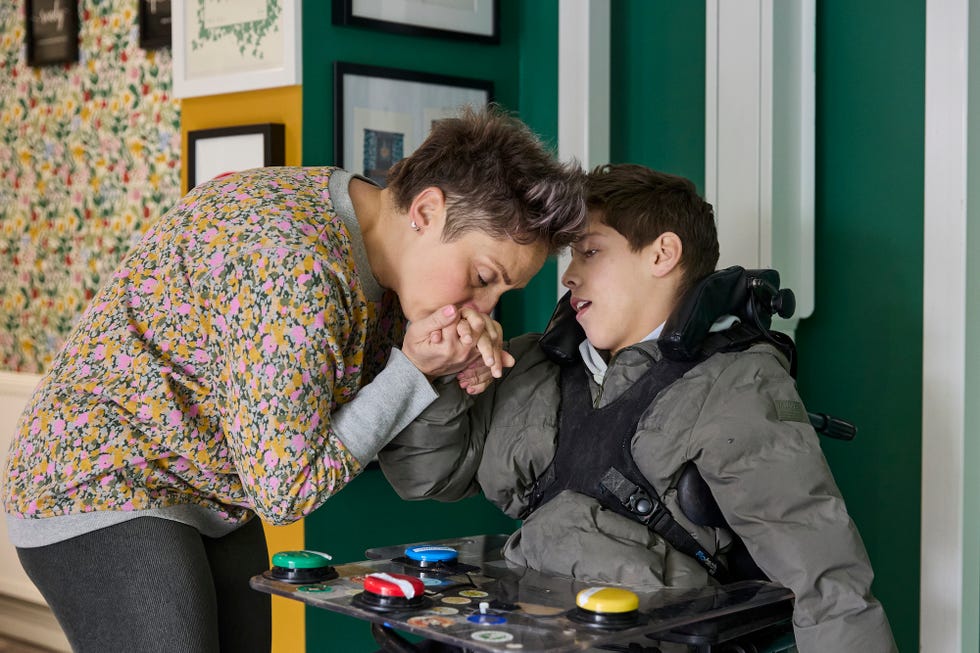 sarah beard kissing her son george on the hand as he sits in his wheelchair