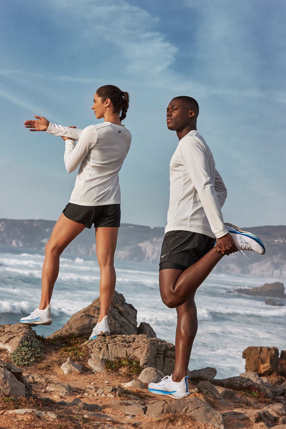 dos personas, hombre y mujer, estiran sobre unas rocas frente al mar