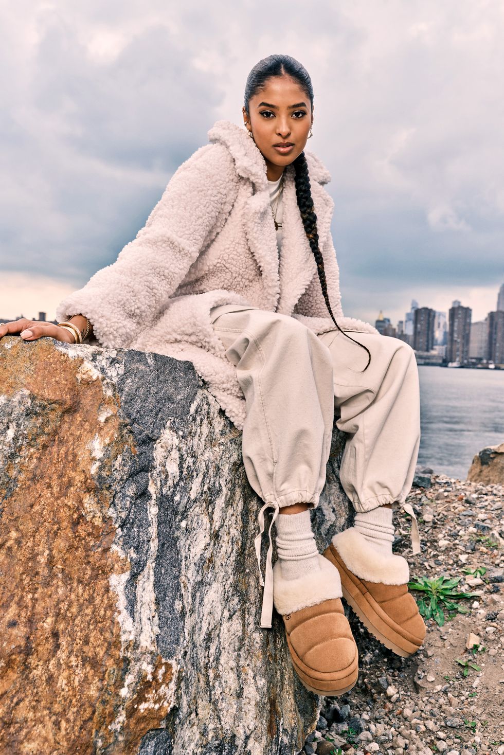 a person in a white coat sitting on a rock with a city in the background