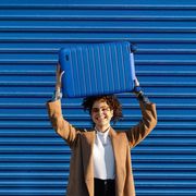 woman holding blue away luggage above head