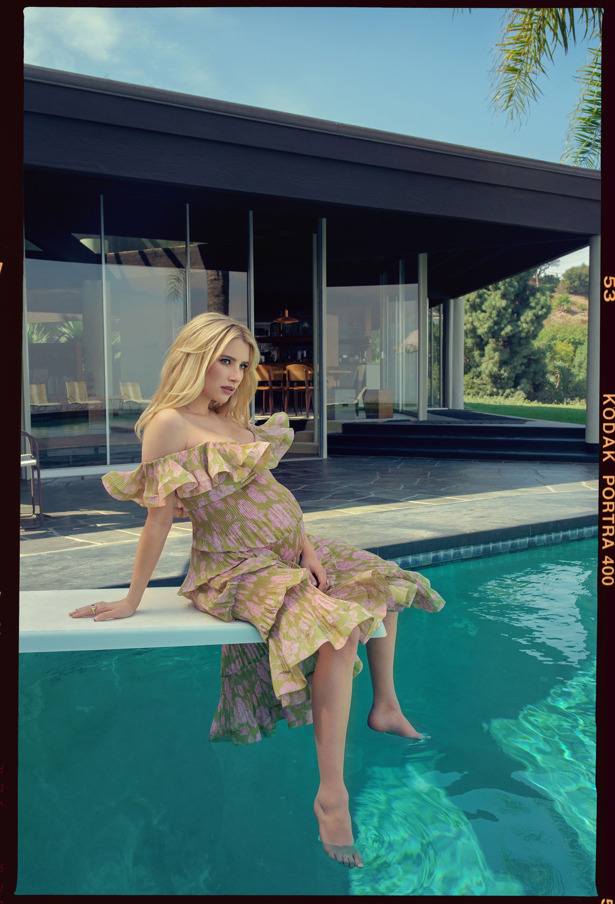 emma roberts, pregnant, wearing a green and pink rose flower dress, sitting on a diving board above pool near home