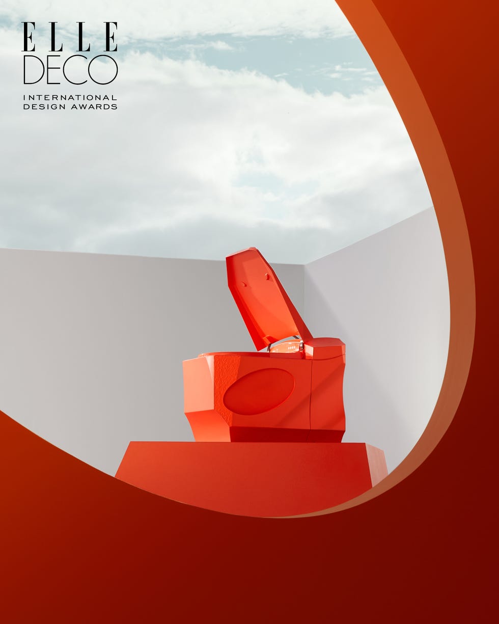 Red sculptural box with lid in a minimalist setting.