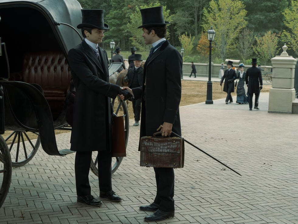 Men in formal attire engaging in a handshake outside a carriage.