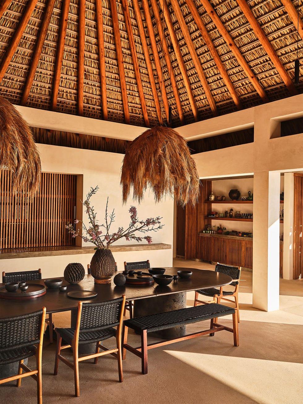 Dining area featuring a large wooden table surrounded by woven chairs and decorative elements.