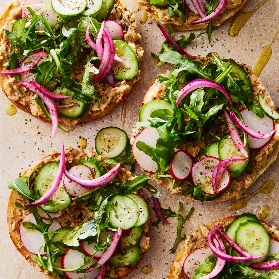 bagel topped with baba ghanoush, sliced cucumber, arugula, and red onions