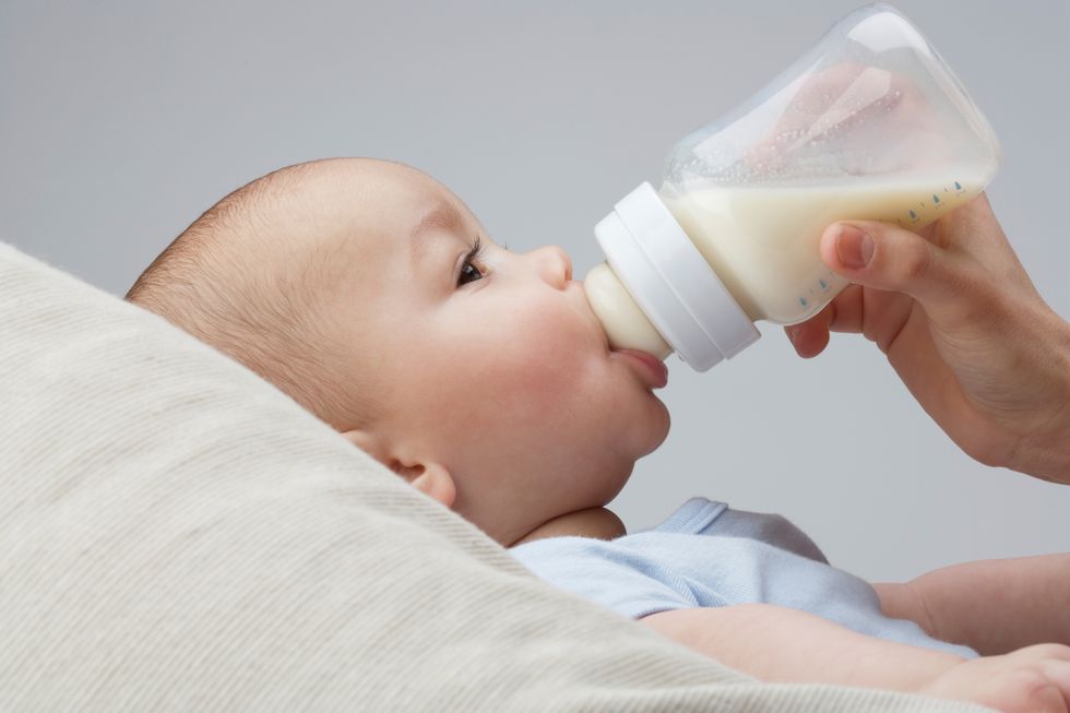 un bebé tumbado en un cojín toma un biberón de leche