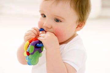 a baby chews on the nuby teether toy which is shaped like a colorful ring of keys, part of a good housekeeping story on the best baby teether toys