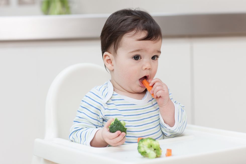 bebé comiendo sólidos como zanahoria y brócoli cocidos sentado en una trona