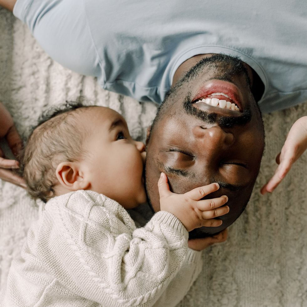 baby boy kissing father lying on blanket at home
