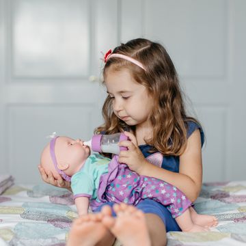 young girl feeding bottle to baby doll on bed