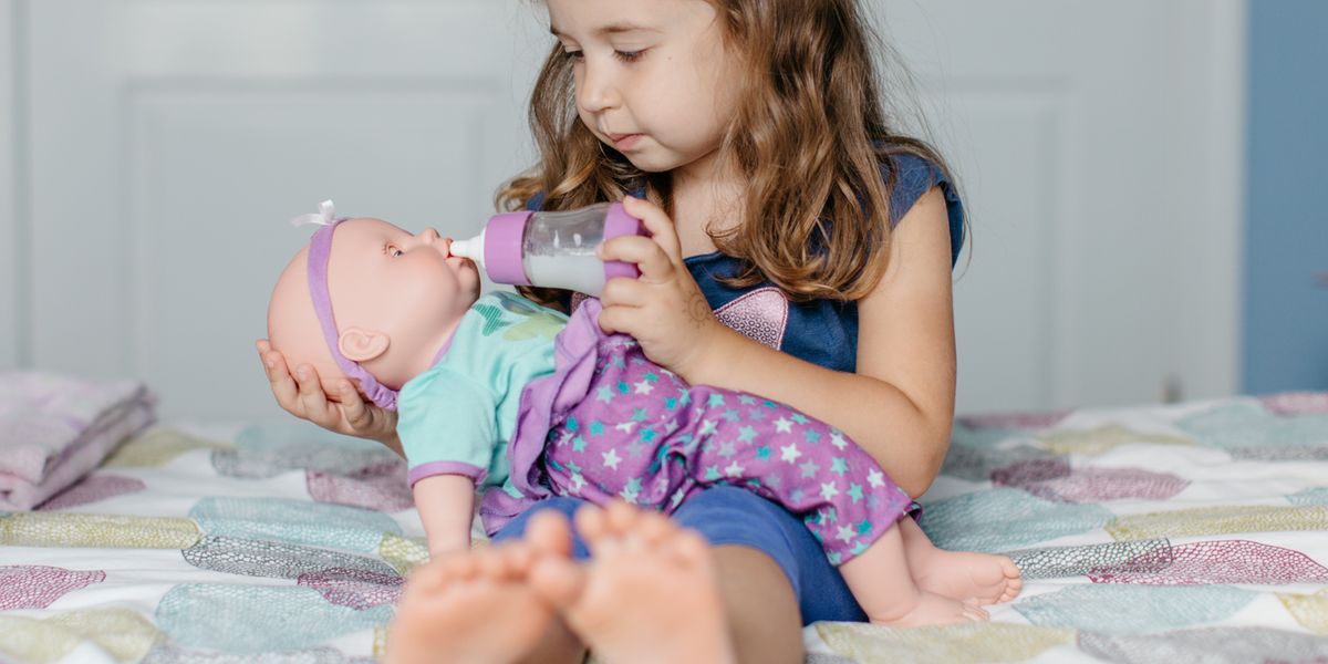 young girl feeding bottle to baby doll on bed