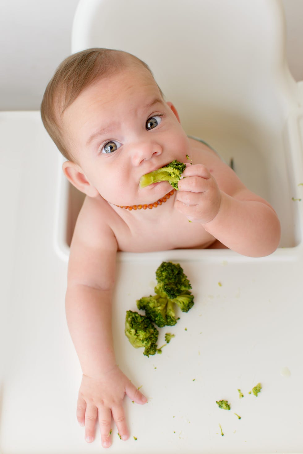 bebé comiendo brócoli en una trona