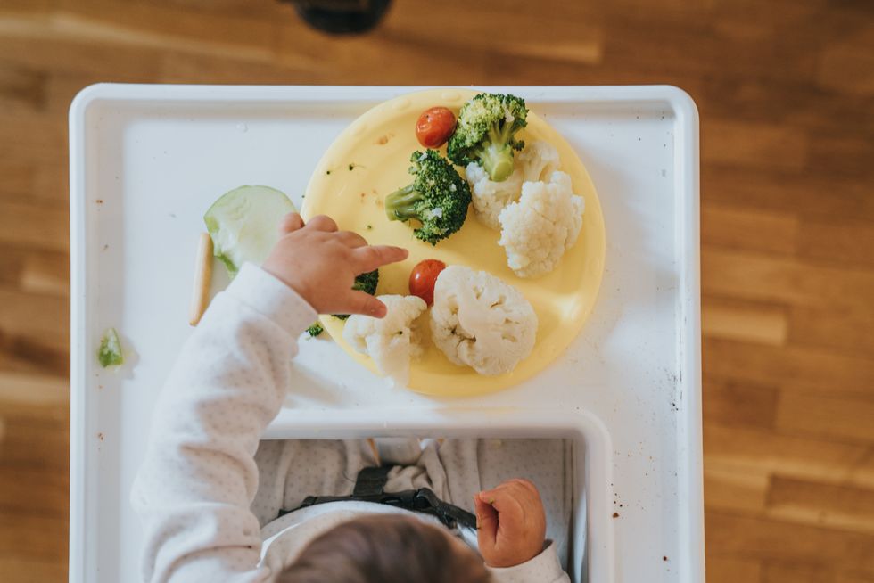 bebé sentado en la trona probando verduras solidas como indica el blw, nueva tendencia en la alimentación complementaria del bebé