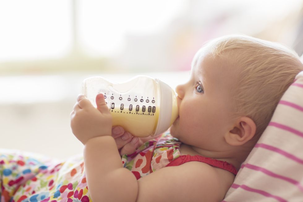 Baby girl drinking from bottle on sofa