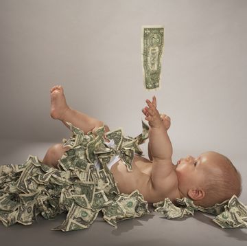 baby girl 5 months lying down covered with us dollar bills falling from above