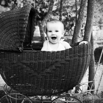 a portrait of a happy baby girl in an antique wicker carriage black and white image with some graininess