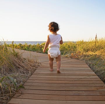 Baby girl (12-15 months) walking on boardwalk amongst grass, rear view baby girl 12 15 months walking on boardwalk amongst grass, rear view