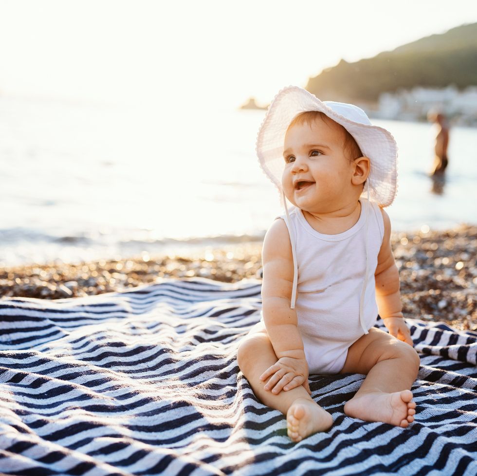 baby girl with hat sitting on towel at the beach in summer