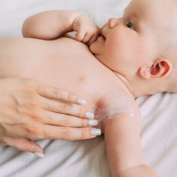 applying baby lotion to arm of infant