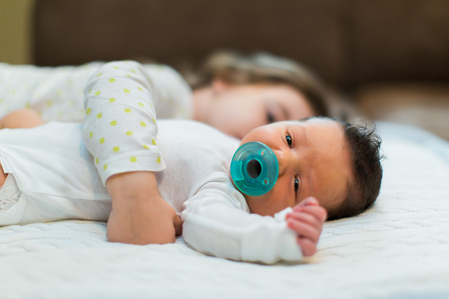 sister hugging infant with pacifier