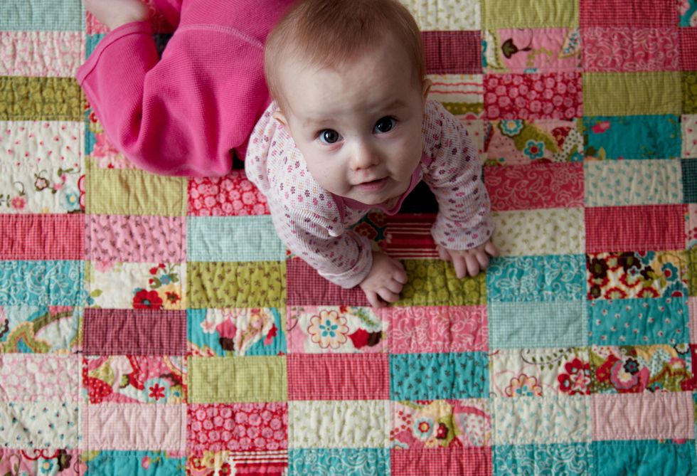 baby girl on a bright handmade patchwork quilt looking up with a small smile