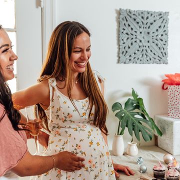 woman touching pregnant belly in front of table at baby shower with gifts and cupcakes