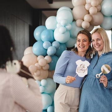 friends pose under a balloon arch as someone takes their photo at a baby shower