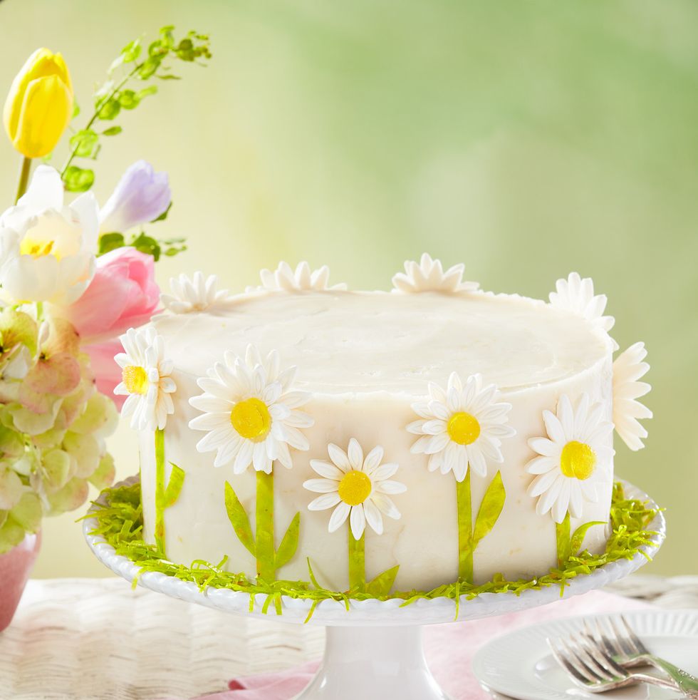 a white cake on a cake stand decorated with yellow and white daisies