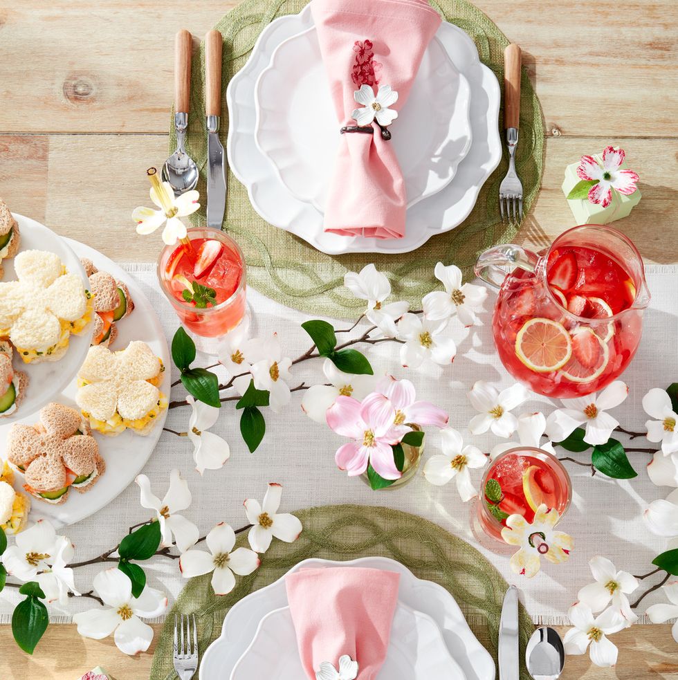 a spring time table setting with dogwood flowers and tea sandwiches and a pink napkin tied up with a flower