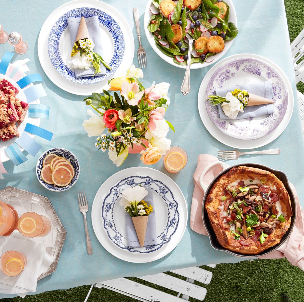 a mostly pink and blue table scape with a dutch baby pastry n an iron skillet and flowers and plates make it all pretty