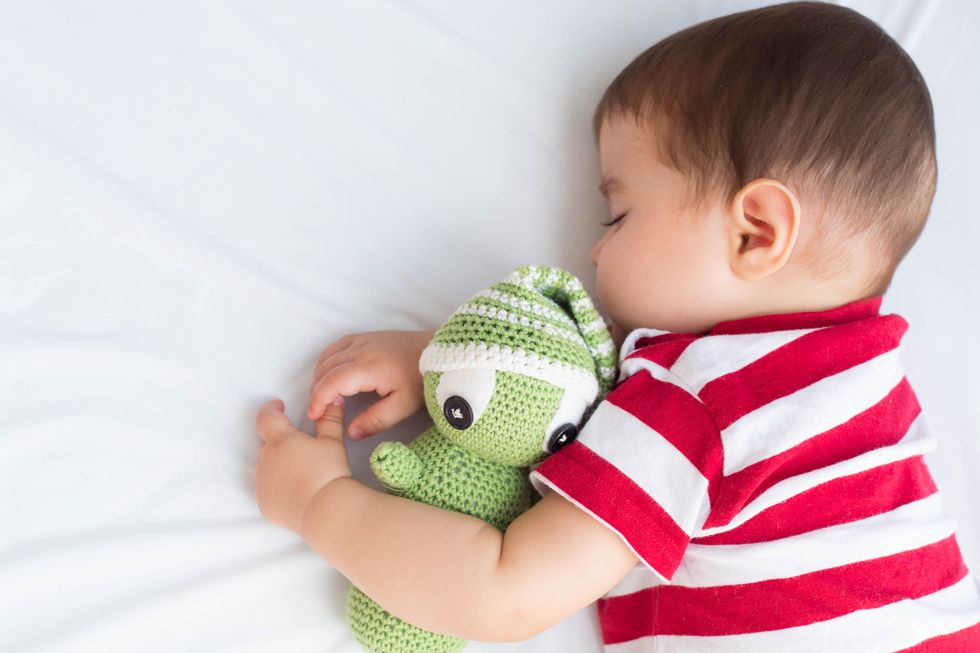 un niño con una camiseta de rayas duerme abrazado a un muñeco de crochet