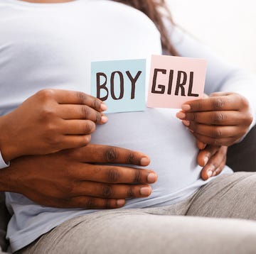 gender reveal concept showing a black pregnant woman holding pink and blue color card for baby boy or girl, with her husband hugging her from behind