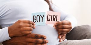 gender reveal concept showing a black pregnant woman holding pink and blue color card for baby boy or girl, with her husband hugging her from behind