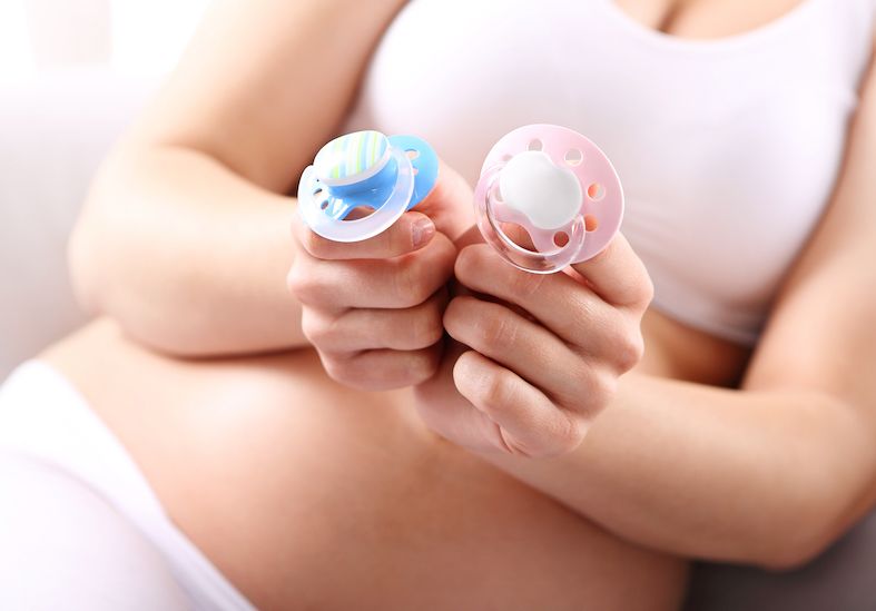 a pregnant woman holding two dummies one is blue to represent a boy and the other is pink to signify being pregnant with a girl