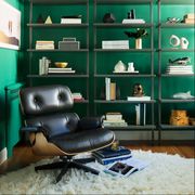 a green study with an eames lounge chair and three shelves with books and other objects
