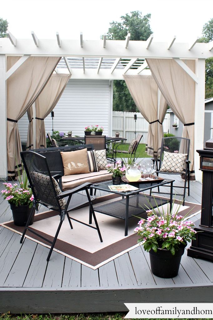 patio pergola with cloth curtains and wrought iron table bench and chairs on a a backyard deck