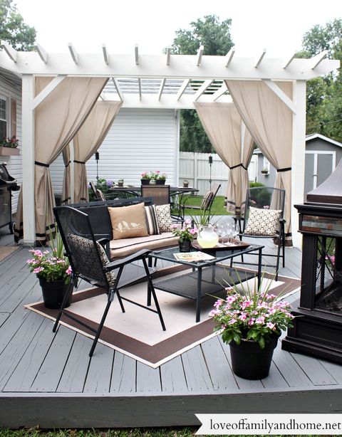 patio pergola with cloth curtains and wrought iron table bench and chairs on a a backyard deck