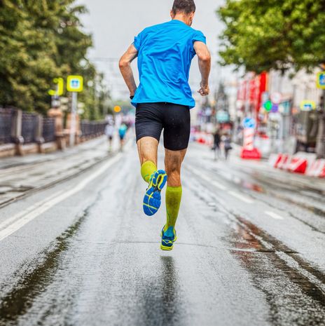 back man athlete running marathon down street in rainy weather