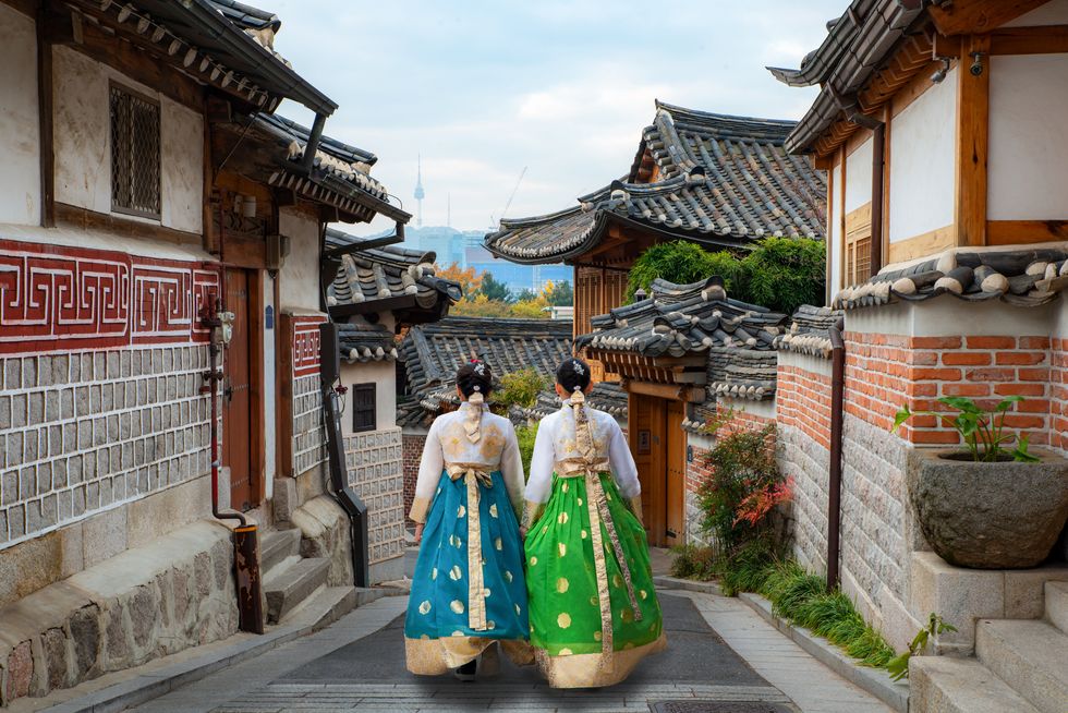 back of two woman wearing hanbok walking through the traditional style houses of bukchon hanok village in seoul, south korea