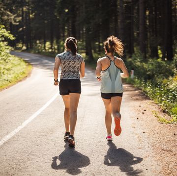 back view of female athletes running on road in forest