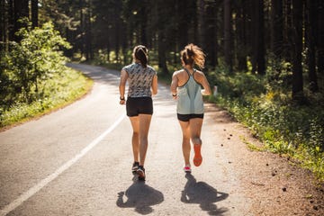 back view of female athletes running on road in forest