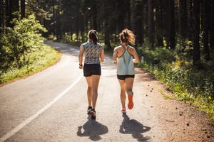 back view of female athletes running Court on road in forest