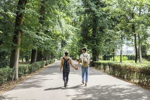 Back view of young gay couple with backpacks walking hand in hand on a road